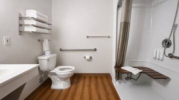 Un baño moderno con inodoro, bidé y zona de ducha, que incluye barras de apoyo y un perchero para toallas.
