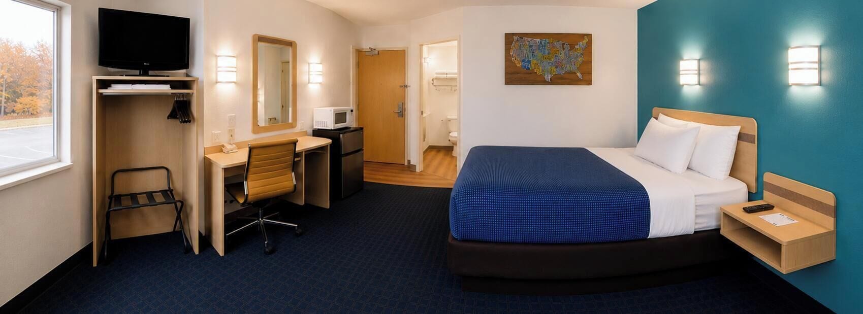 Una habitación de hotel con cama, escritorio, silla, televisor y un cuadro en la pared.