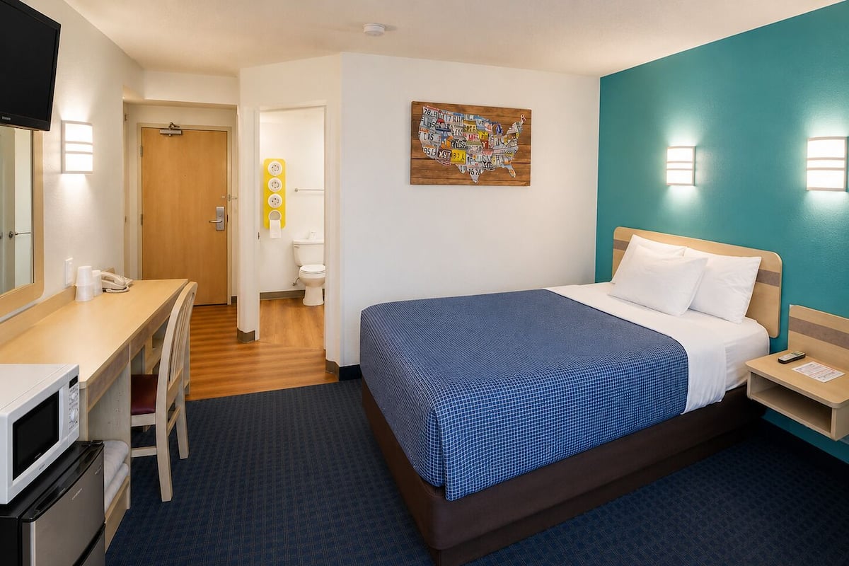 A hotel room with a bed, desk, chair, and a television.