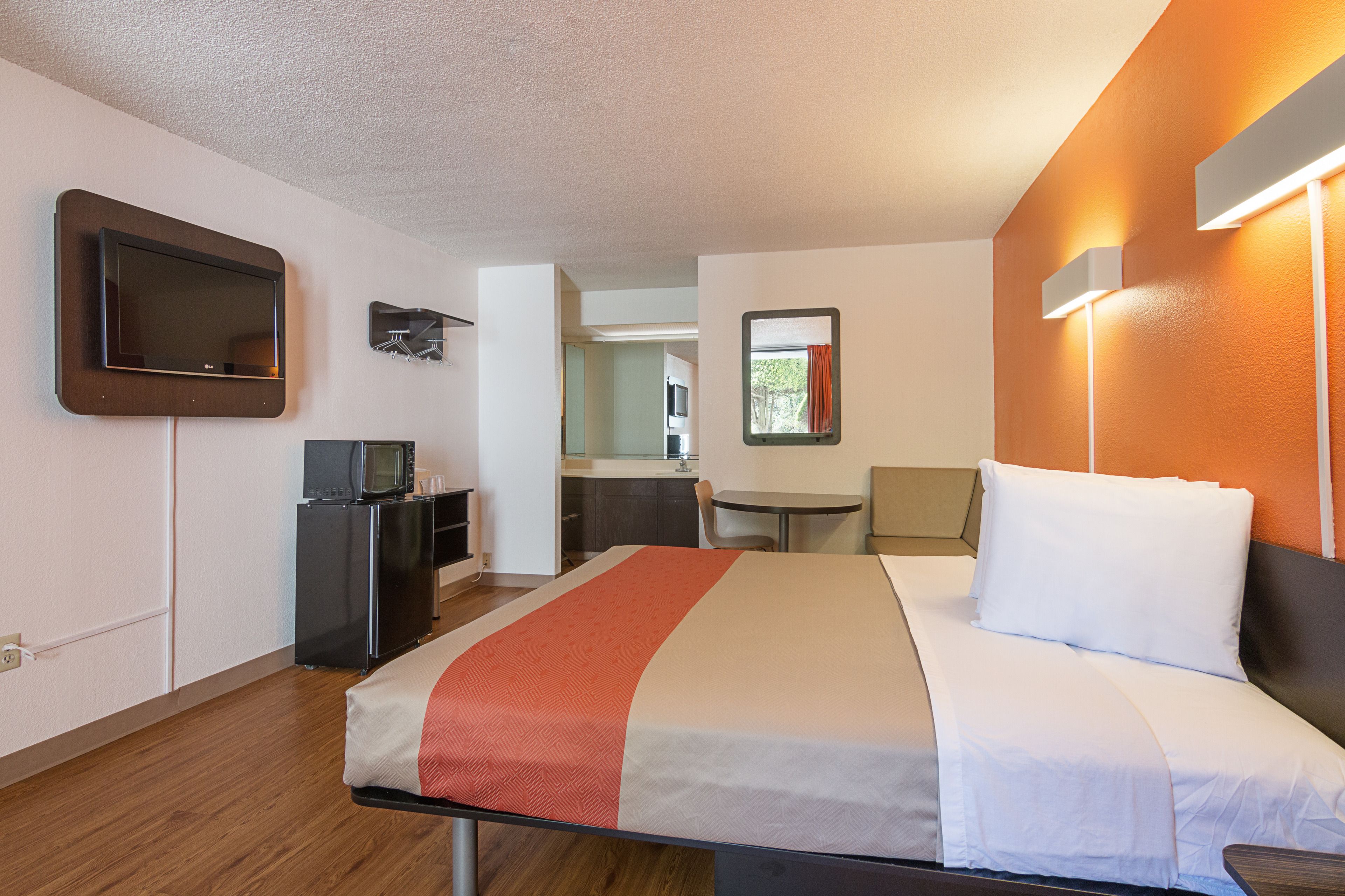 Una habitación de hotel con una cama, un escritorio con computadora, televisor y una kitchenette pequeña.