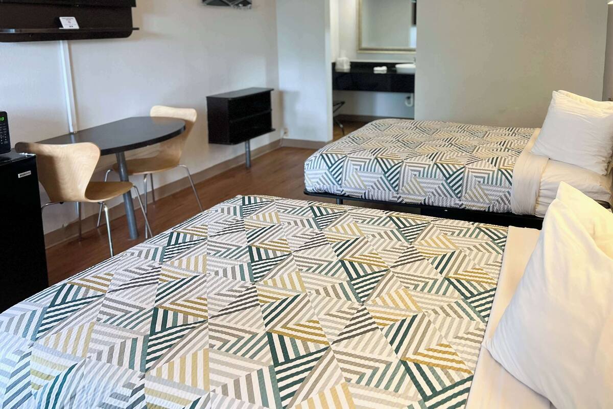 A hotel room with two beds, a desk, a chair, a TV, and a bathroom visible in the background.