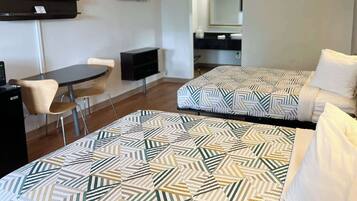 A hotel room with two beds, a desk, a chair, a TV, and a bathroom visible in the background.