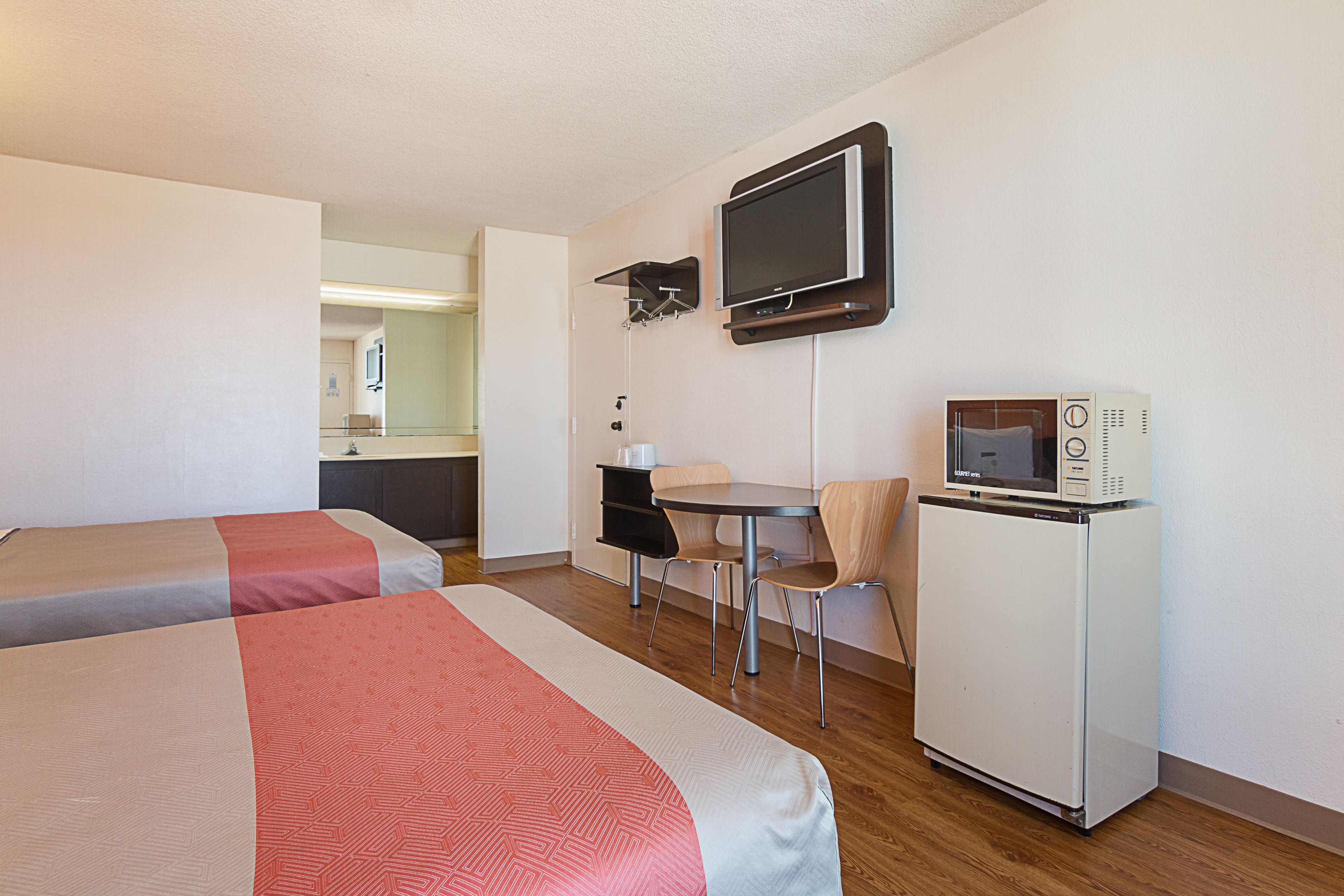 A hotel room with two beds, a small kitchenette, a TV, and a microwave.