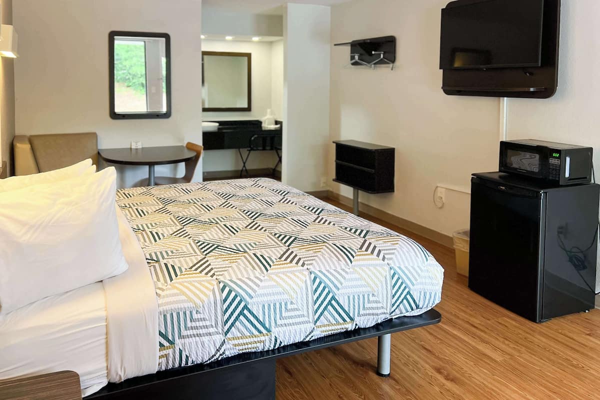 A hotel room with a bed, a desk, a chair, a TV, and a microwave.