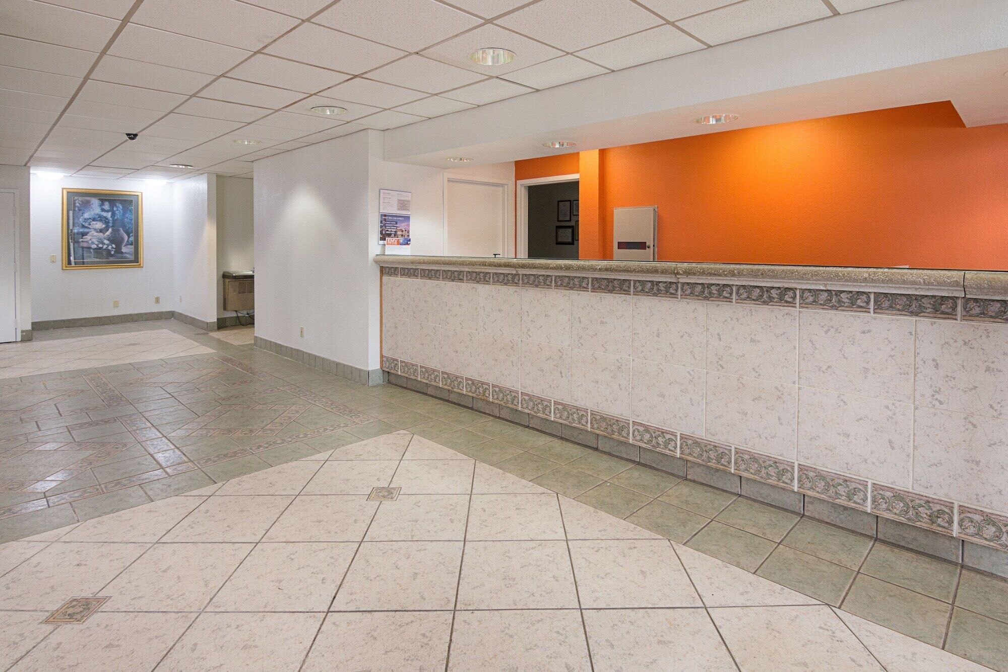 A hotel lobby with a reception desk, tiled flooring, and a framed picture on the wall.