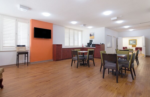 A dining area with wooden flooring, a TV mounted on the wall, and a painting on the wall.