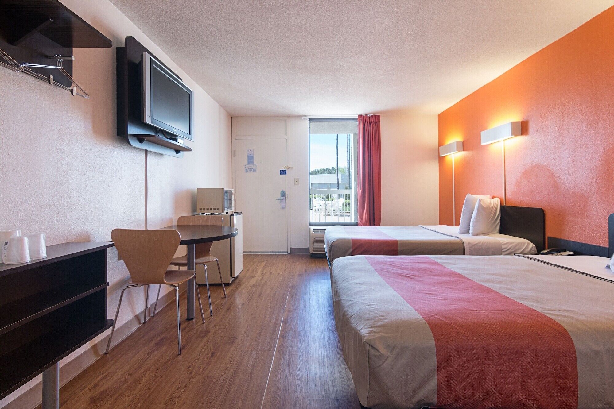 A hotel room with two beds, a desk, a television, and a window with curtains.