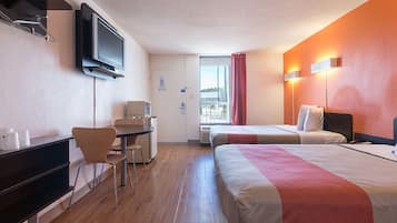 A hotel room with two beds, a desk, a television, and a window with curtains.