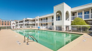 A pool area with a clear pool, white poolside chairs, and a building with multiple balconies.