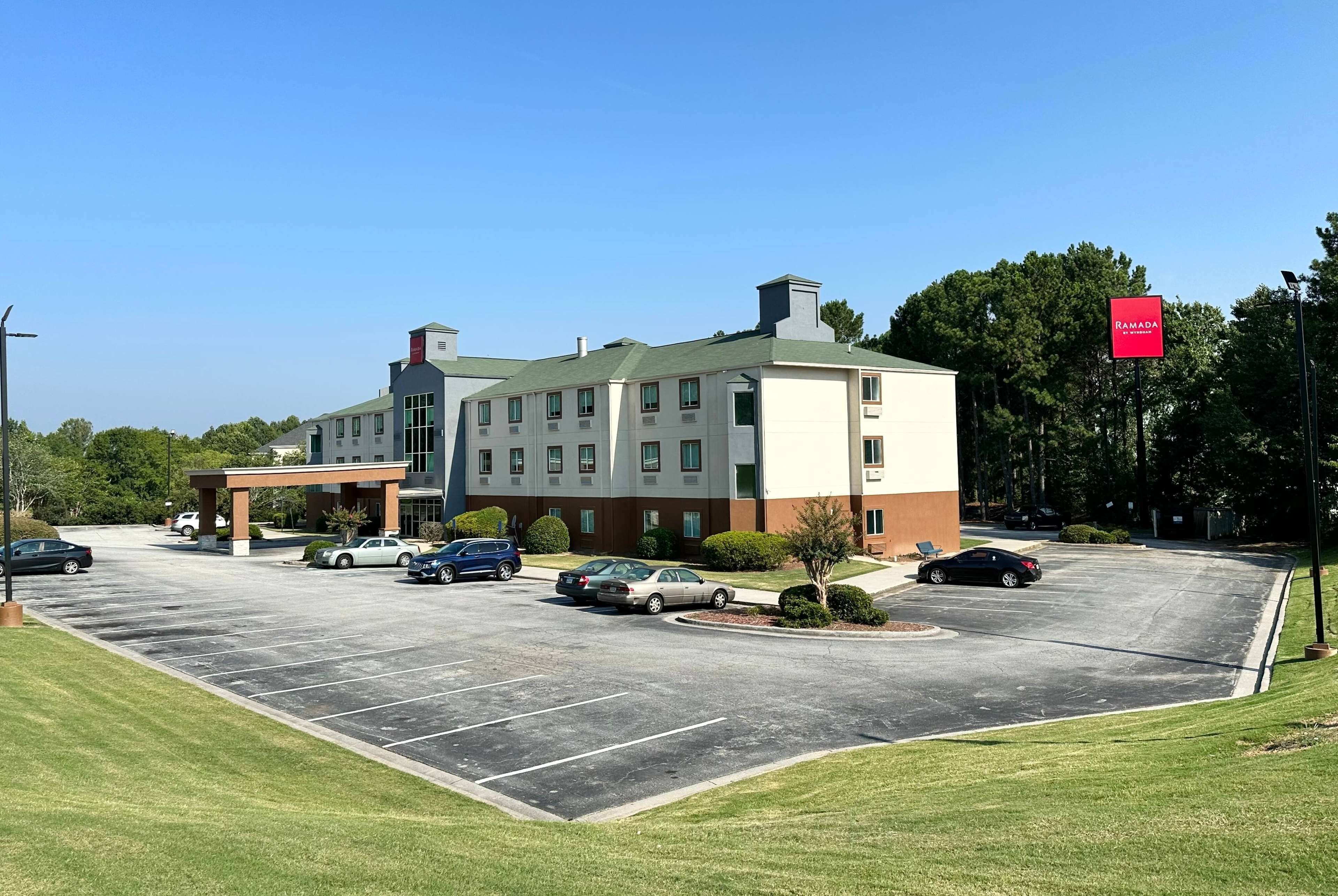 A multi-story hotel with a parking lot, a covered entrance, and a sign indicating a Ramada Inn.