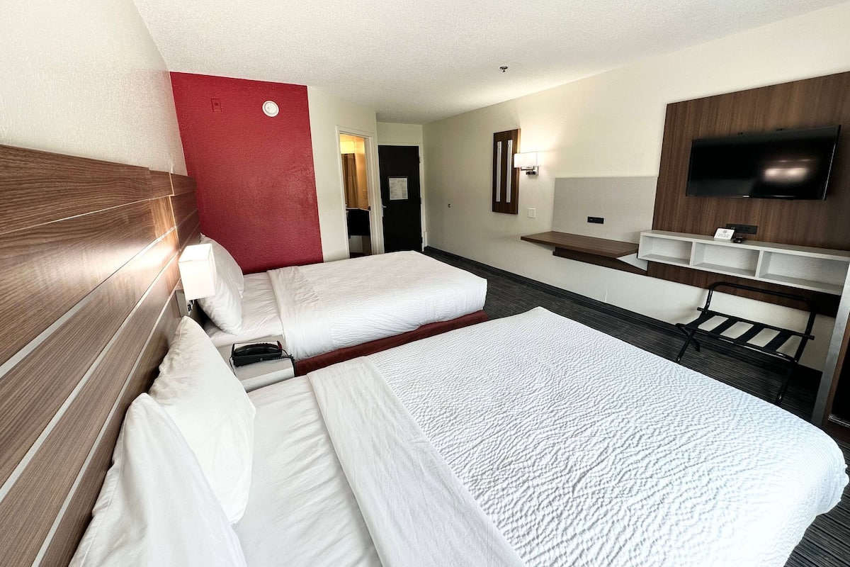 A hotel room with two beds, a TV, a desk, and a mirror.