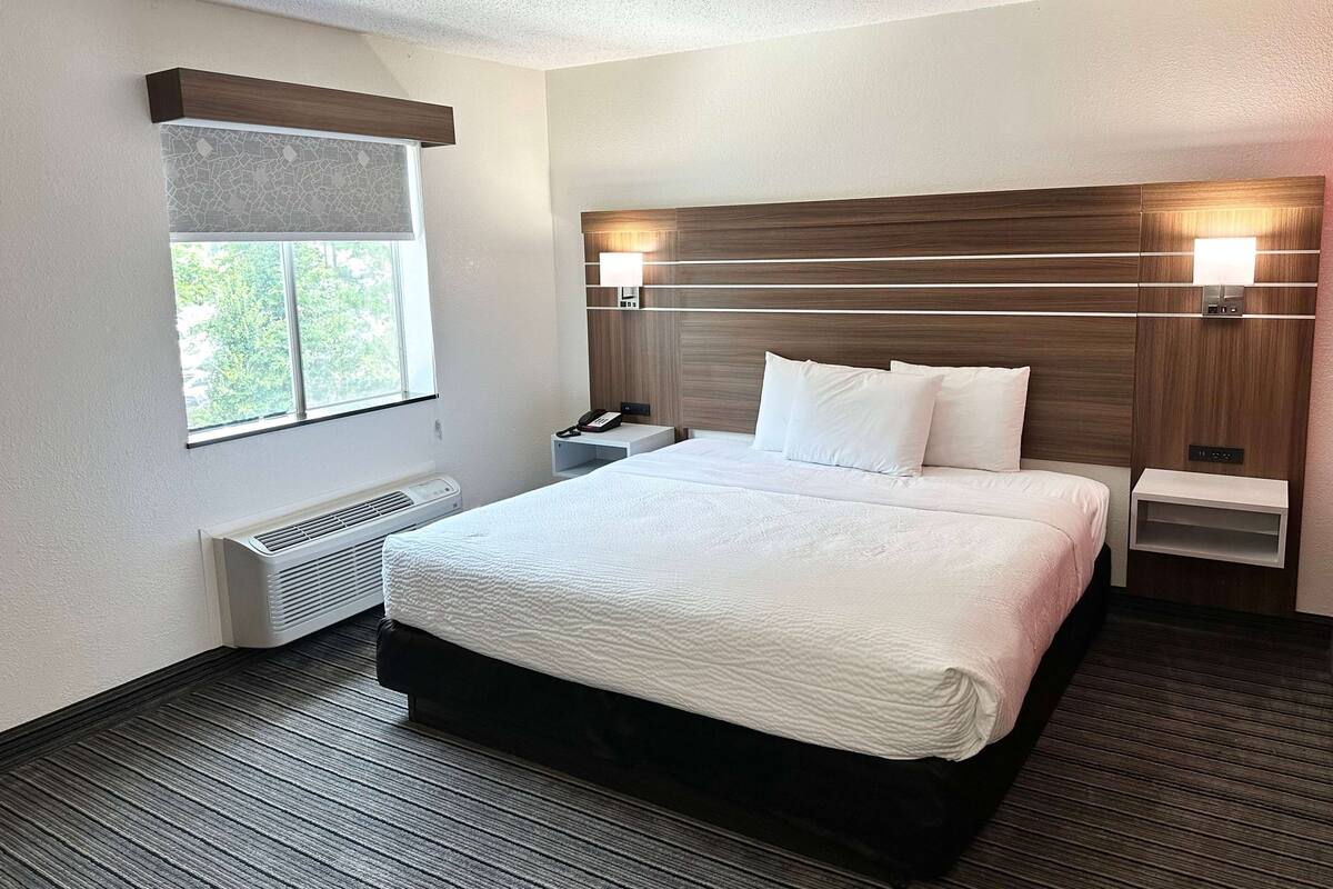 A hotel room with a large bed, bedside lamps, a telephone, and a window with blinds.