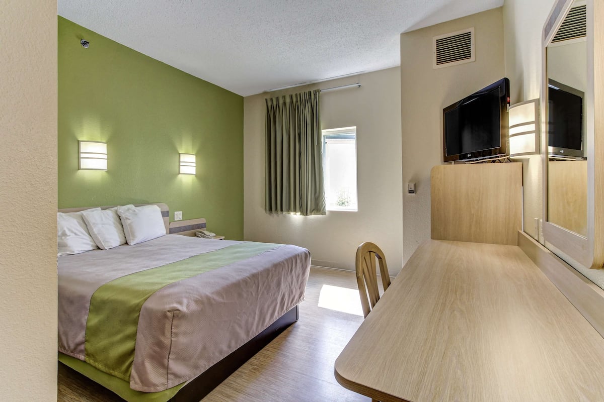 Ein Hotelzimmer mit einem Bett, einem Schreibtisch, einem Fernseher und einem Fenster mit Vorhängen.