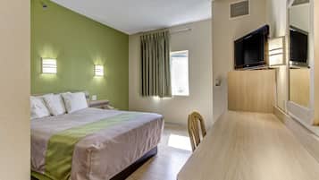 A hotel room with a bed, a desk, a television, and a window with curtains.