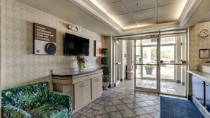 A reception area with a sofa, a TV, a clock, and a sign about morning charge. - Motel 6 Medina, OH - Cleveland (Medina)