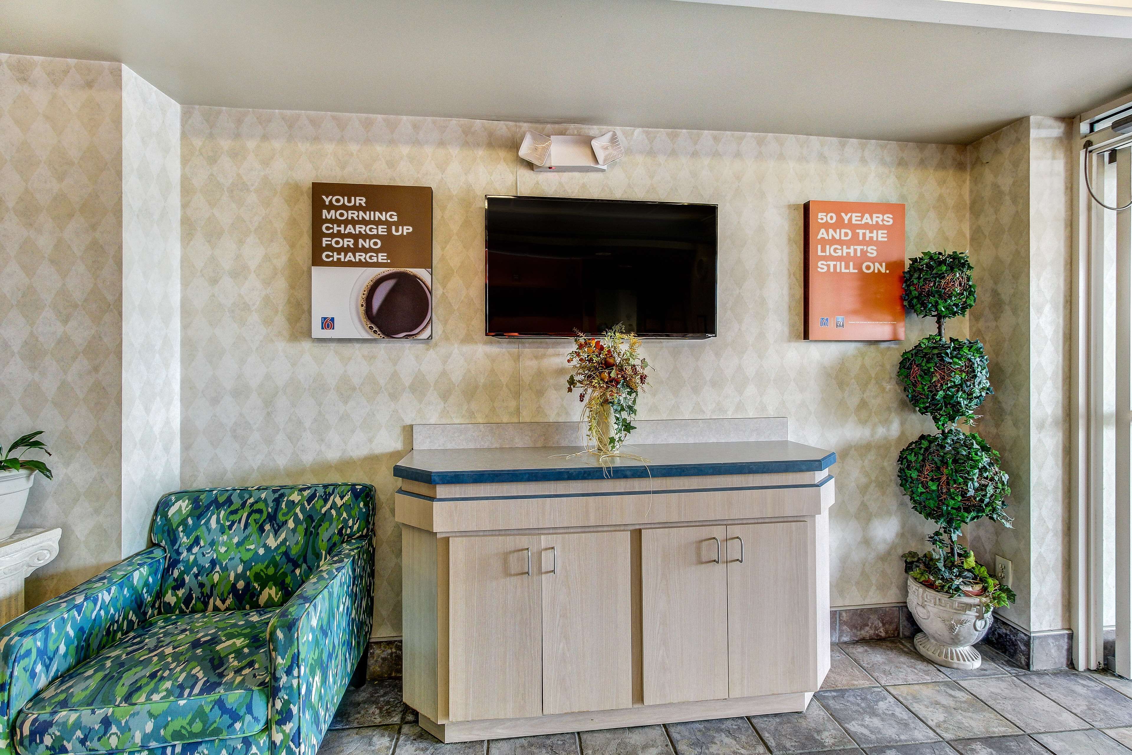 A room with a TV mounted on the wall, a cabinet with a vase of flowers, and a patterned chair.