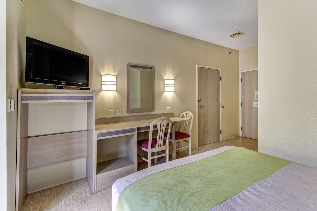 Ein Hotelzimmer mit einem Bett, einem Schreibtisch mit Stuhl, einem Fernseher und zwei Wandleuchten.