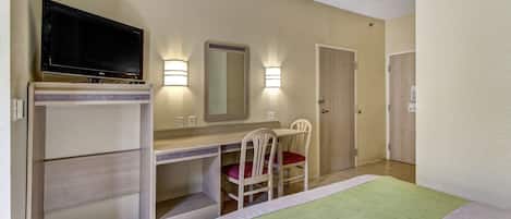A hotel room with a bed, a desk with a chair, a television, and two wall-mounted lights.