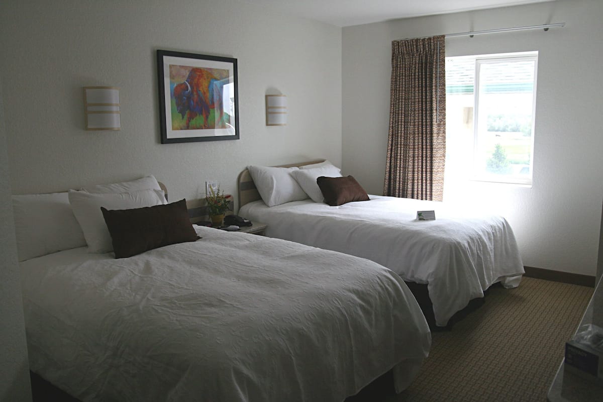 Una habitación de hotel con dos camas, un cuadro en la pared y una ventana con cortinas.