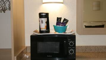 A black West Bend microwave on a kitchen counter with a coffee maker and a teal bowl containing coffee pods.