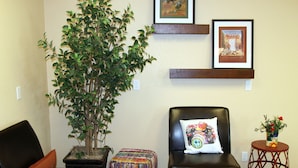 A living room with a black leather sofa, a small wooden table with a vase, a potted plant, and two colorful woven ottomans. - Buffalo Inn (Buffalo)