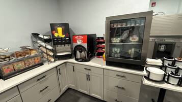 Una kitchenette con cafetera, refrigerador y dispensador de café.