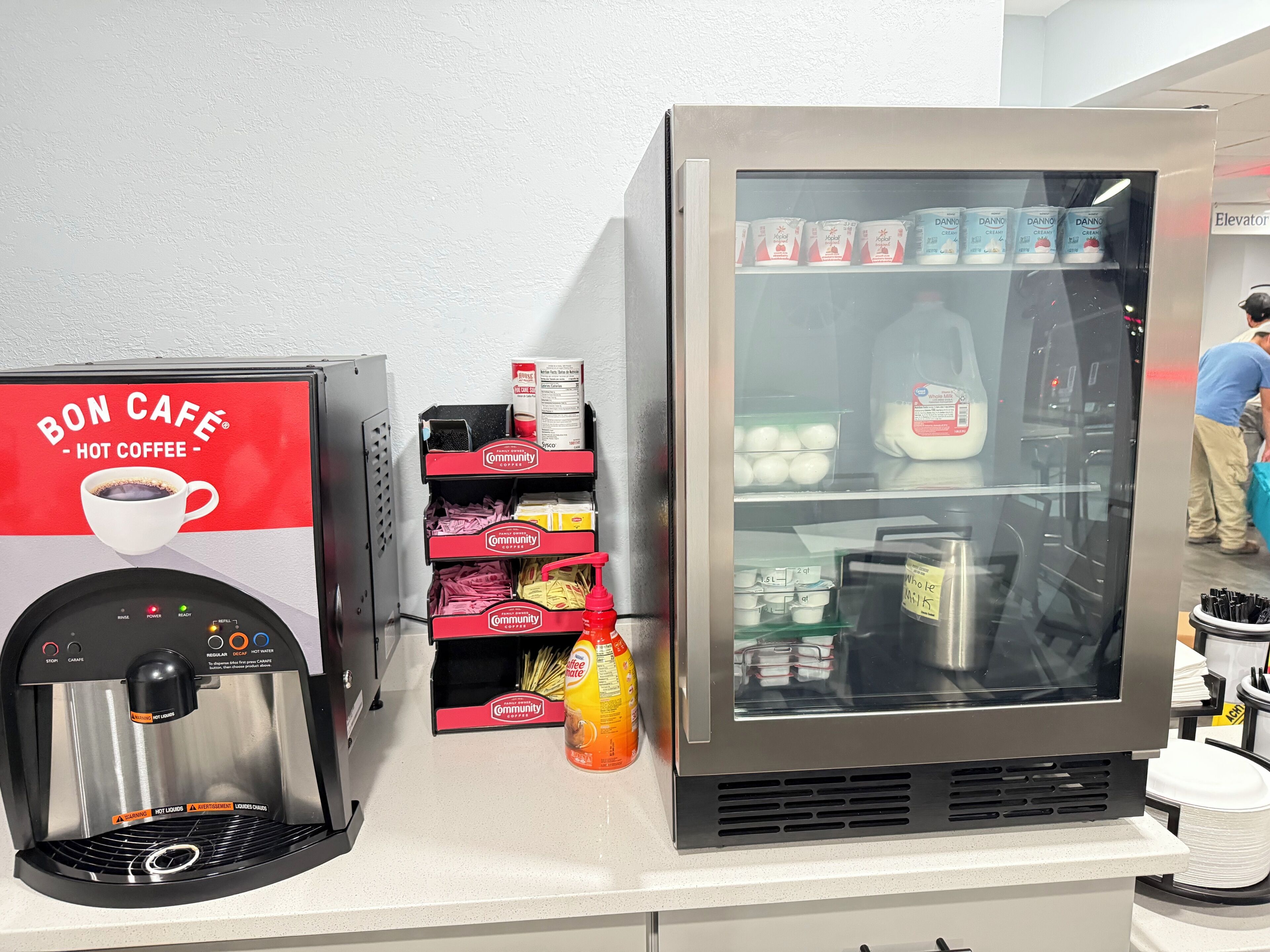 A coffee machine and a refrigerated display with various dairy products.