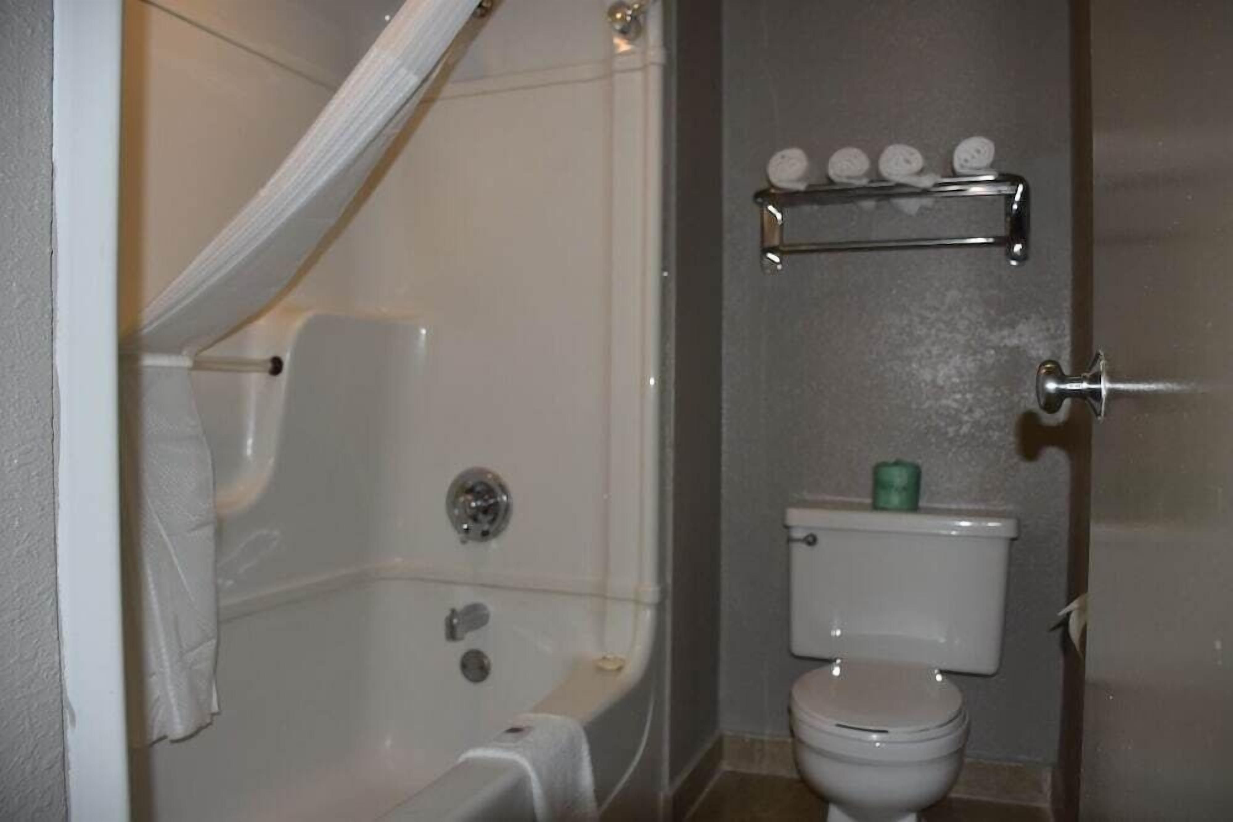 A bathroom with a bathtub, toilet, and a shelf with toiletries.