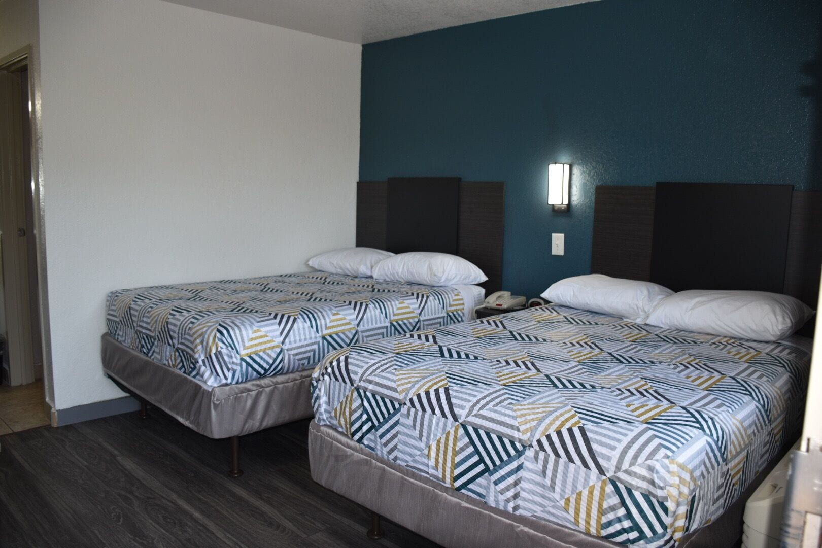 A hotel room with two beds, each with patterned bedding, a nightstand, and a wall-mounted light.