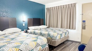 A hotel room with two beds, a blue accent wall, a window with curtains, and a door with a security lock. - Studio 6 Grand Prairie, TX (Grand Prairie)