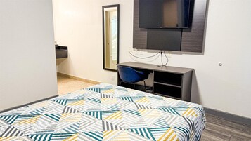 Una habitación de hotel con una cama, un escritorio, una silla, un televisor y un espejo.