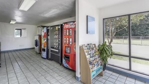 Una máquina expendedora de Coca-Cola, un tablón de anuncios y una ventana con vistas a un campo deportivo.