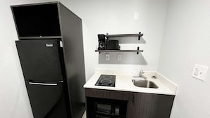 Una cocina compacta con un refrigerador negro, un microondas, un fregadero y una pequeña encimera.