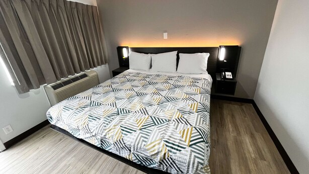 Una habitación de hotel con una cama, una mesita de noche, una lámpara y una ventana con cortinas.