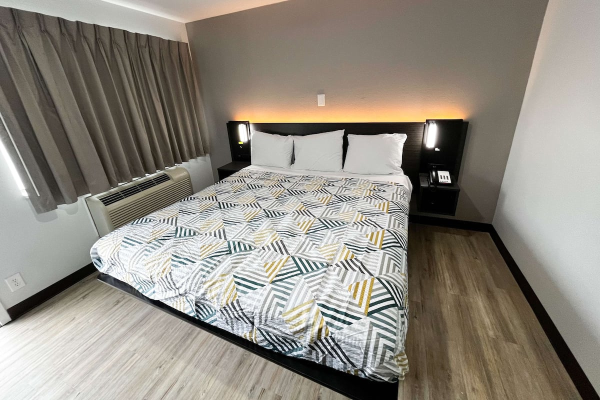 A hotel room with a bed, a nightstand, a lamp, and a window with curtains.