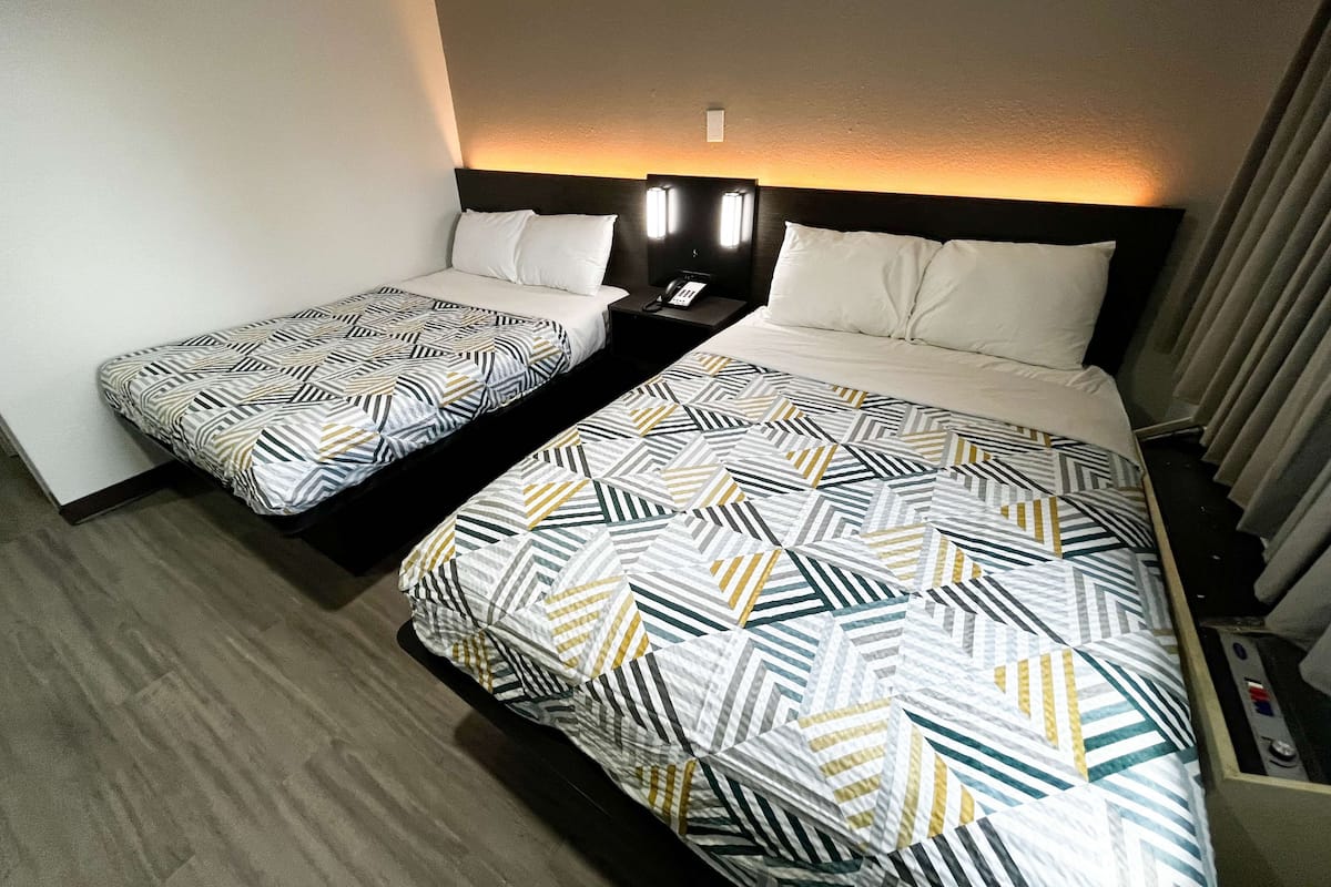 A hotel room with two beds, each with patterned bedding. There is a nightstand with a phone and a lamp between the beds.