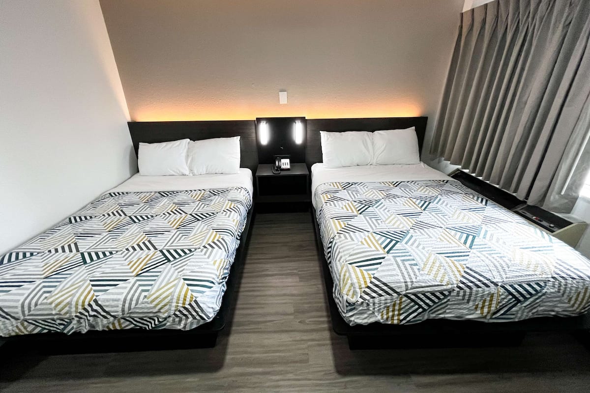 A hotel room with two single beds, a nightstand with a phone, and a window with curtains.