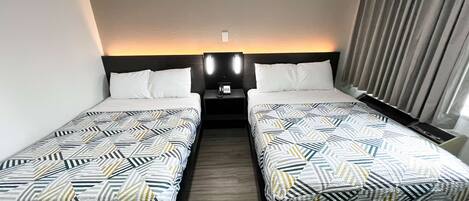 Une chambre d’hôtel avec deux lits simples, une table de chevet avec un téléphone et une fenêtre avec des rideaux.