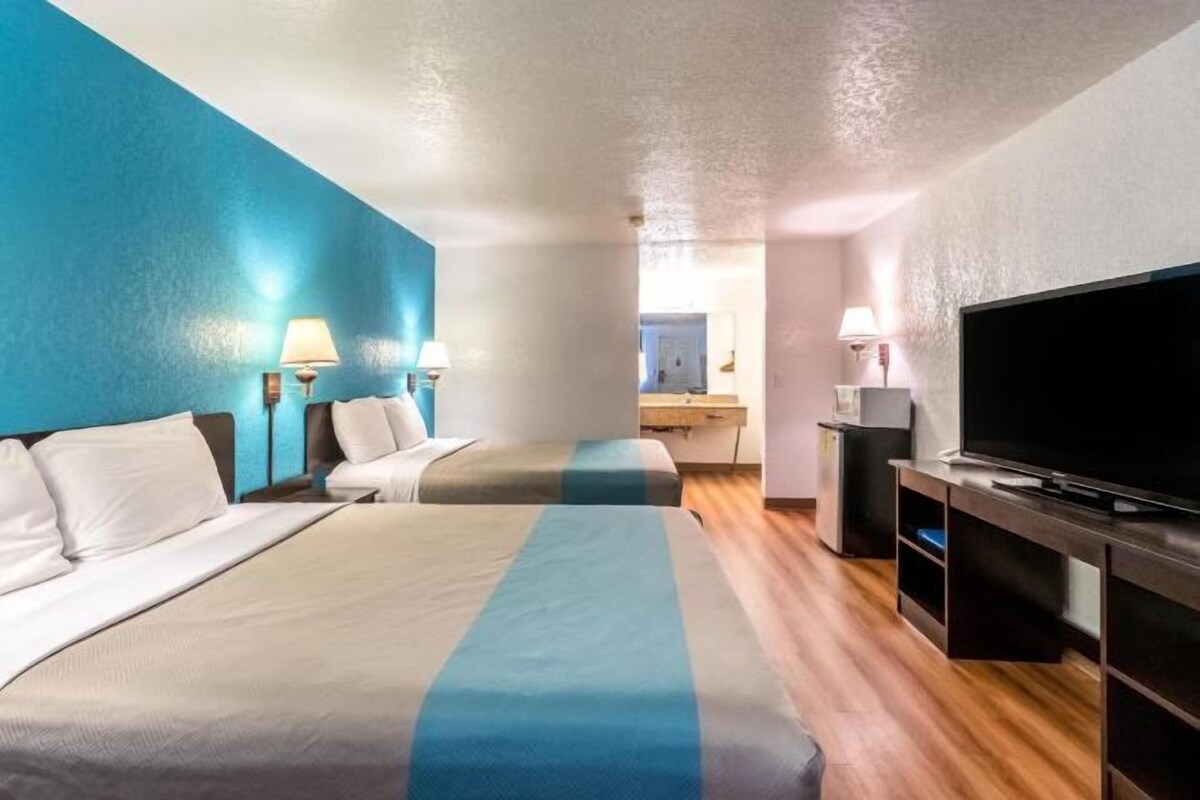 A hotel room with two beds, a TV, and a desk with a lamp.
