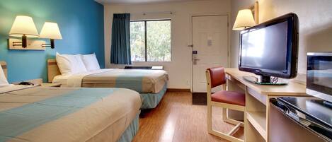 A hotel room with two beds, a desk with a television, and a chair.