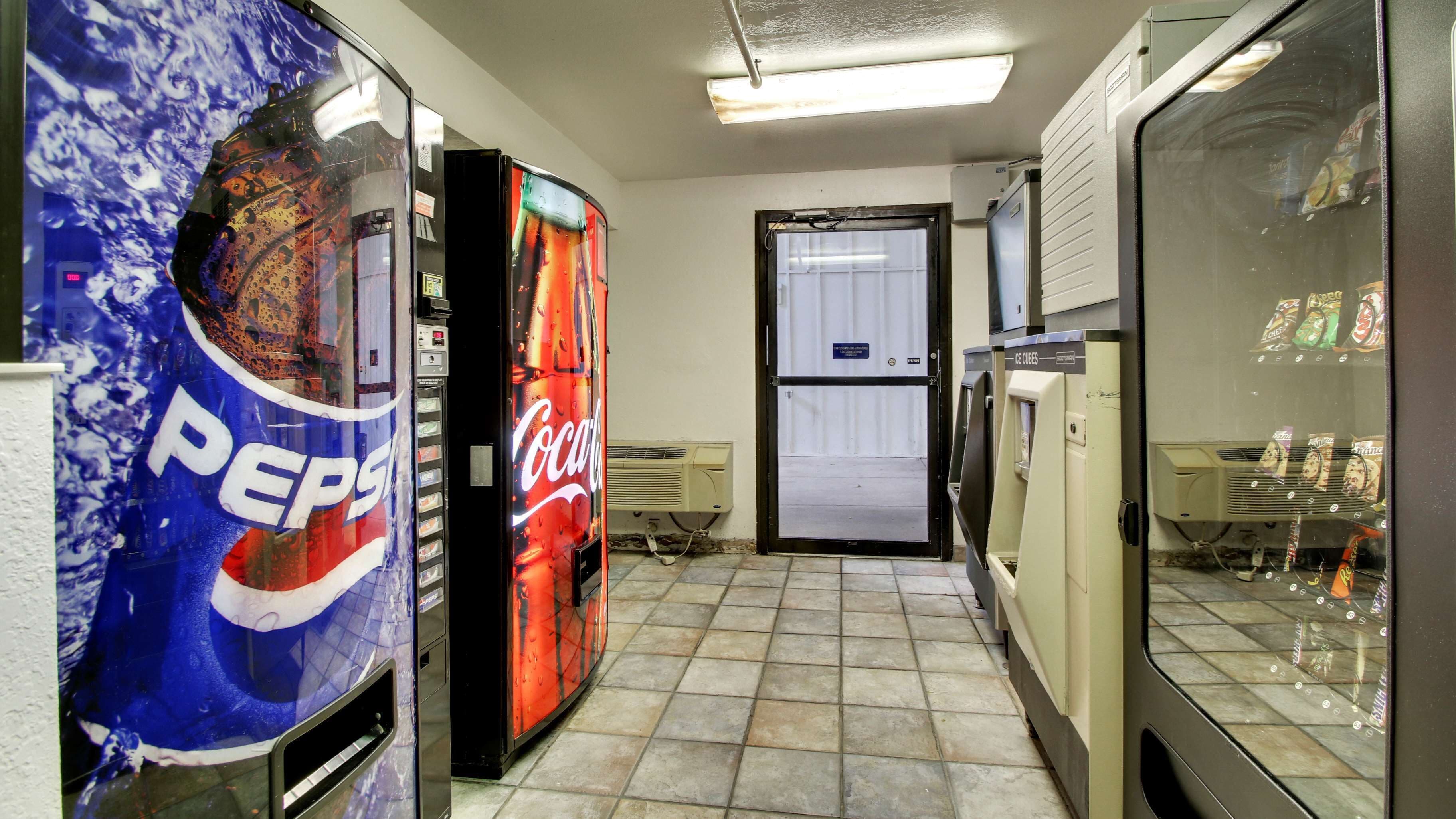 A hallway with vending machines, including Pepsi and Coca-Cola, and a door leading to another room.