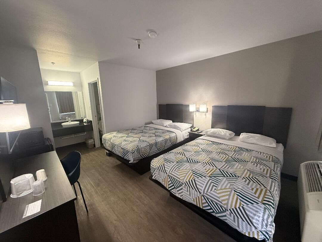 A hotel room with two beds, a desk, a chair, a mirror, and a bathroom visible through an open door.