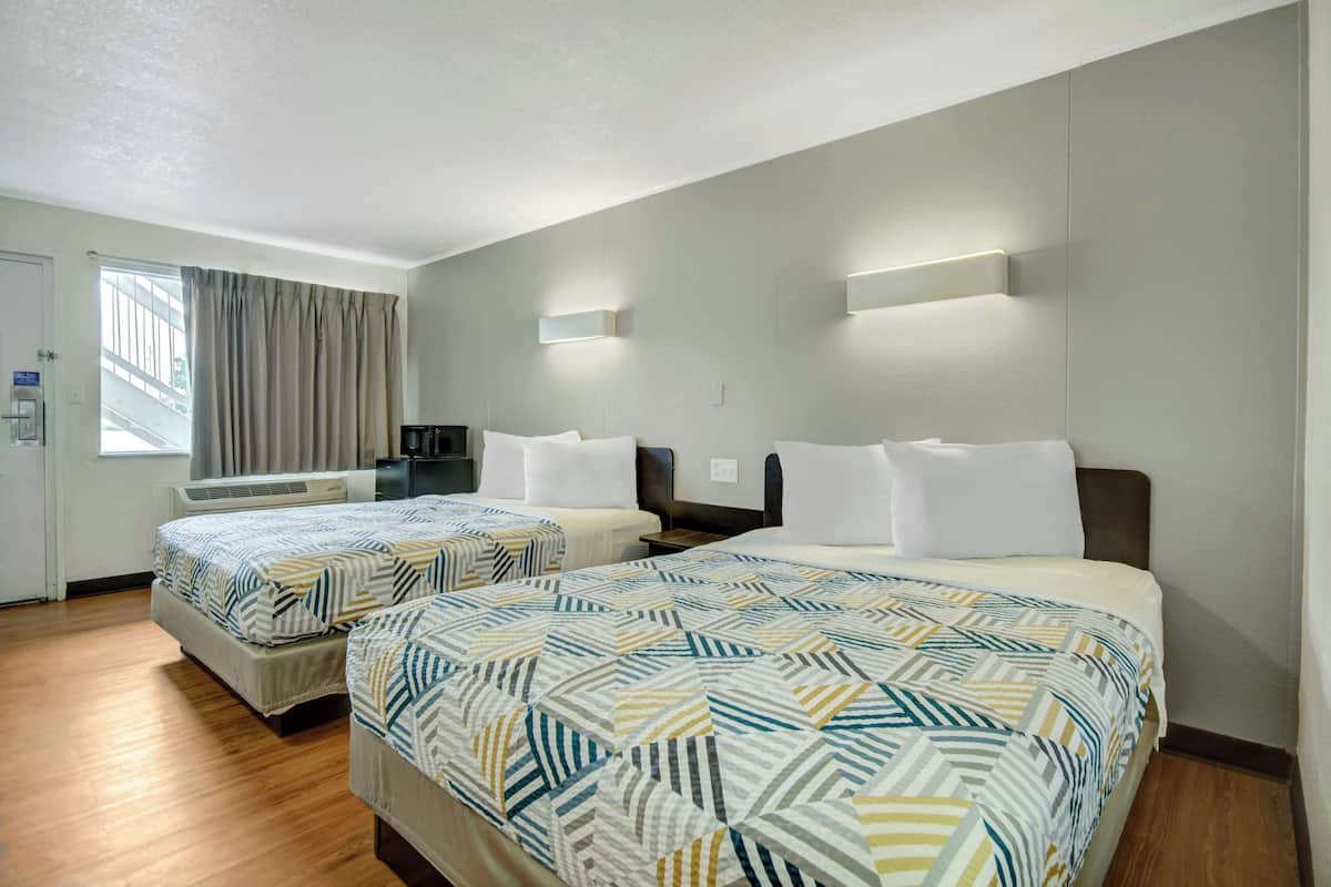 A hotel room with two beds, a desk, and a window with curtains.