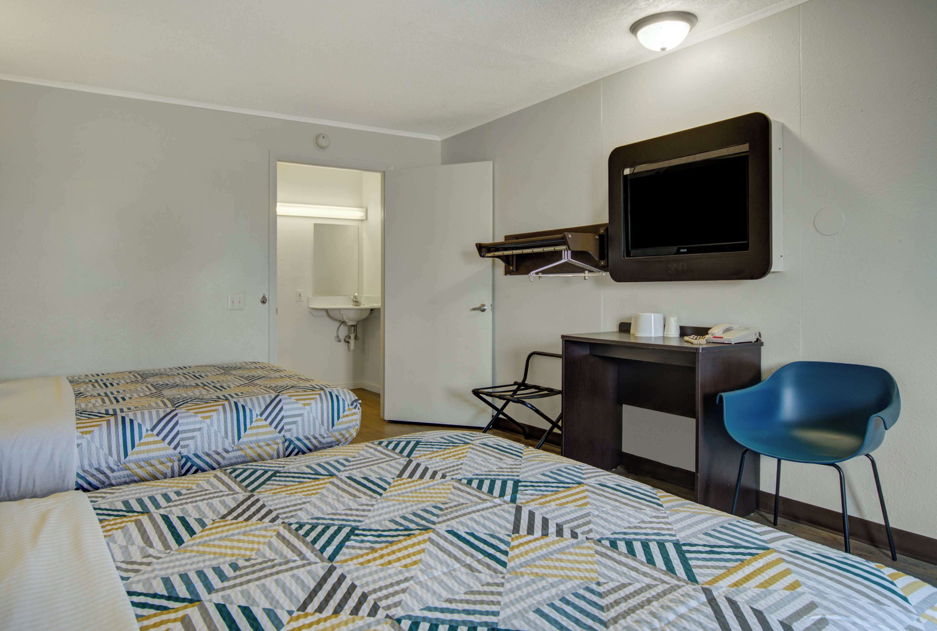 A hotel room with two beds, a desk, a chair, a mirror, and a television.