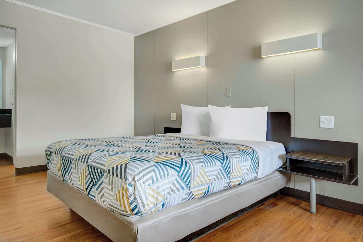 A modern hotel room with a large bed, a bedside table, and a wall-mounted light fixture.