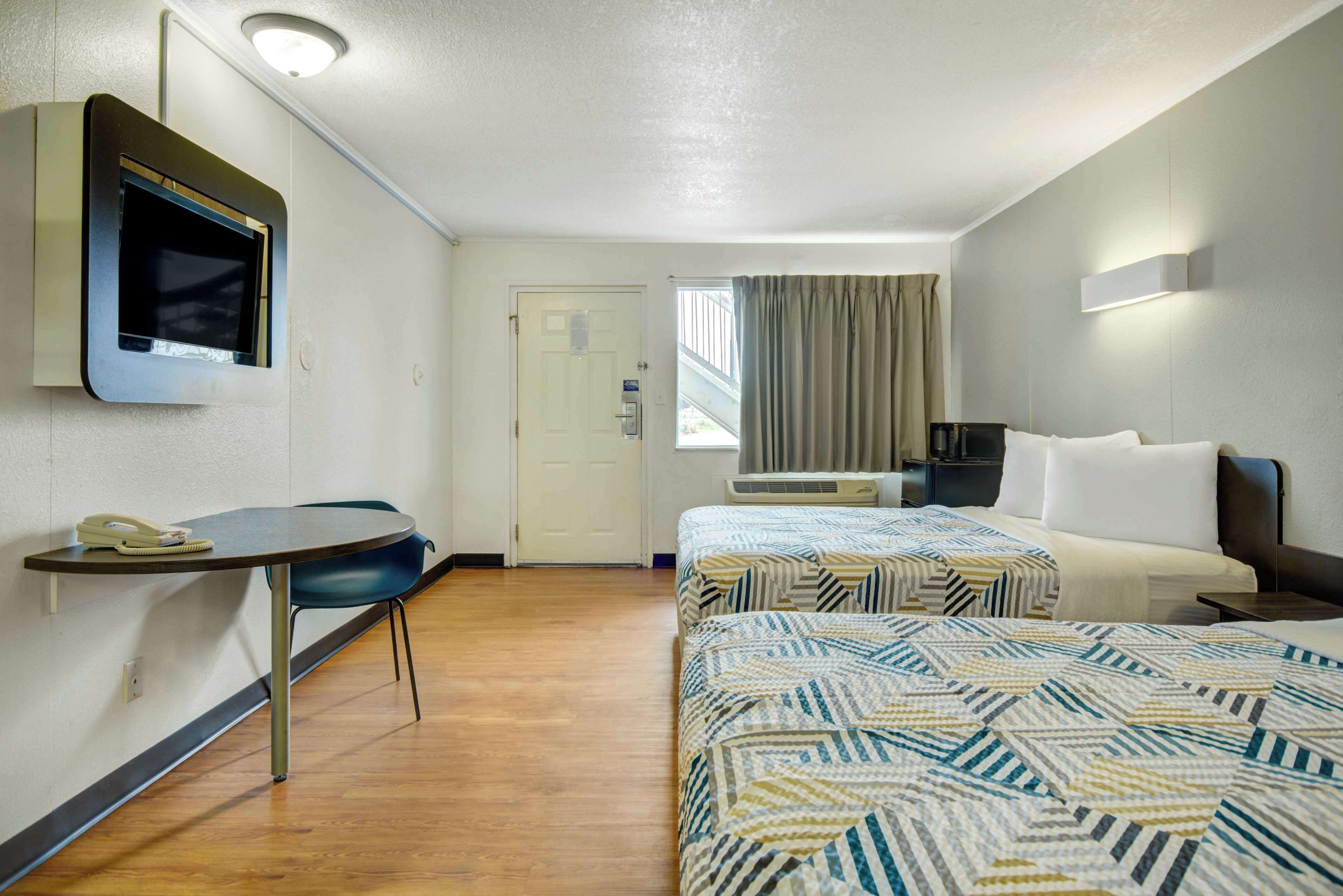 A hotel room with two beds, a desk with a telephone, a TV mounted on the wall, and a window with curtains.