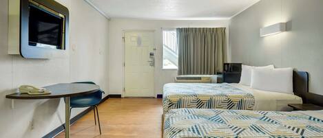 A hotel room with two beds, a desk with a telephone, a TV mounted on the wall, and a window with curtains.