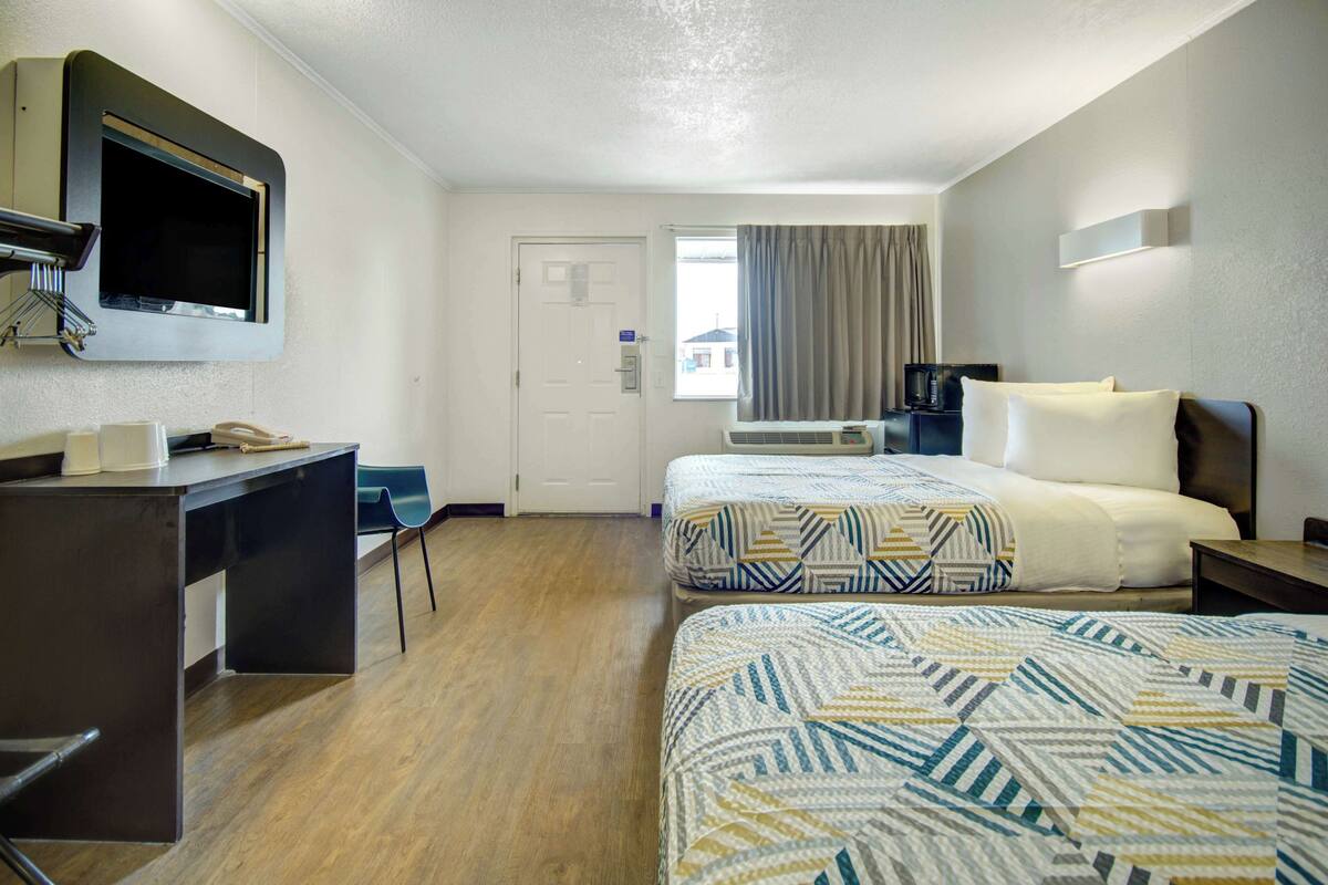 A hotel room with two beds, a desk, a TV, and a window with curtains.