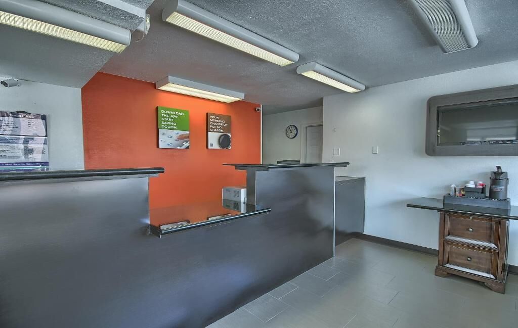 Un área de recepción con diseño moderno, que incluye un mostrador de recepción, un reloj y un mueble bajo con objetos encima.