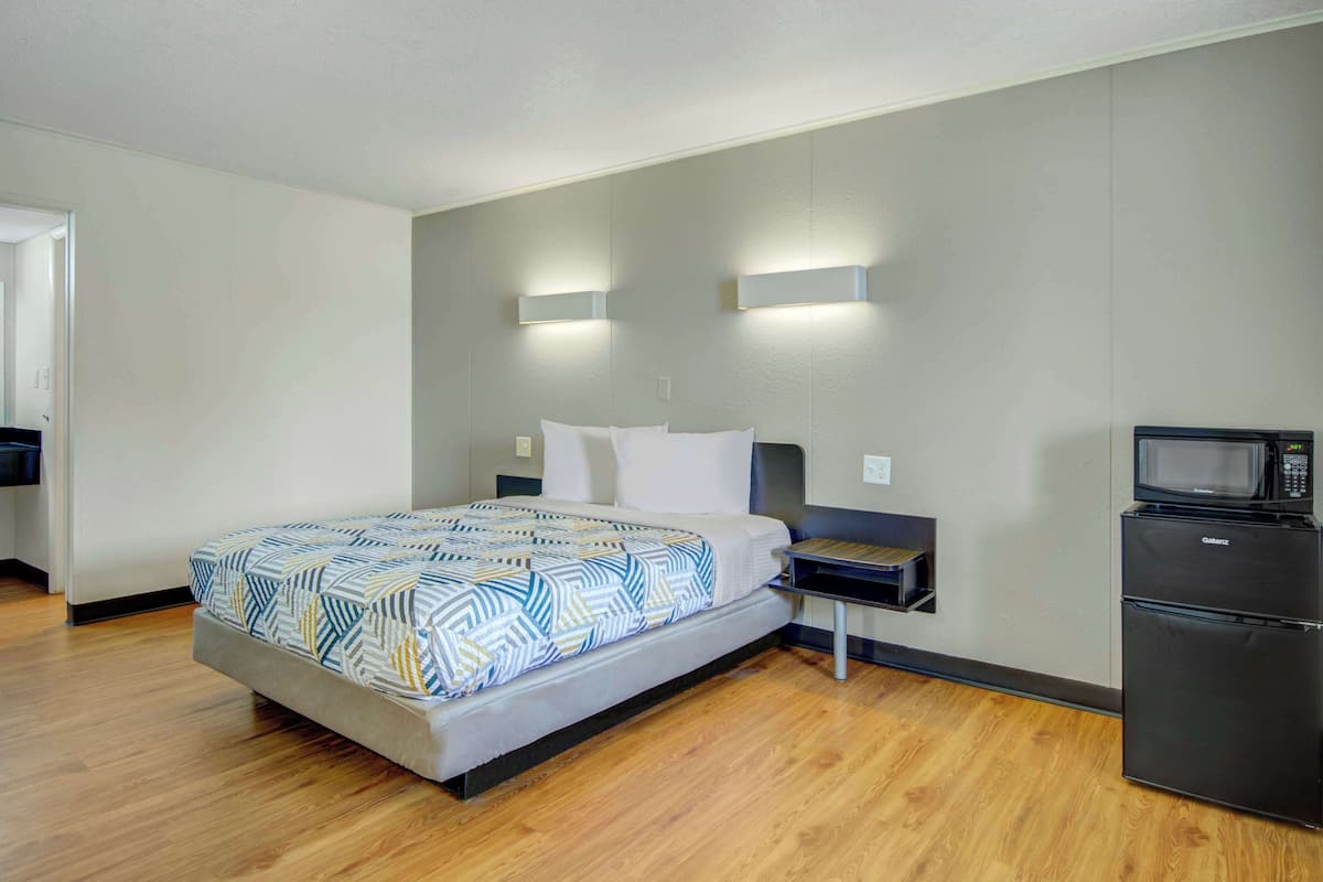 A modern hotel room with a bed, bedside tables, a microwave, and a refrigerator.